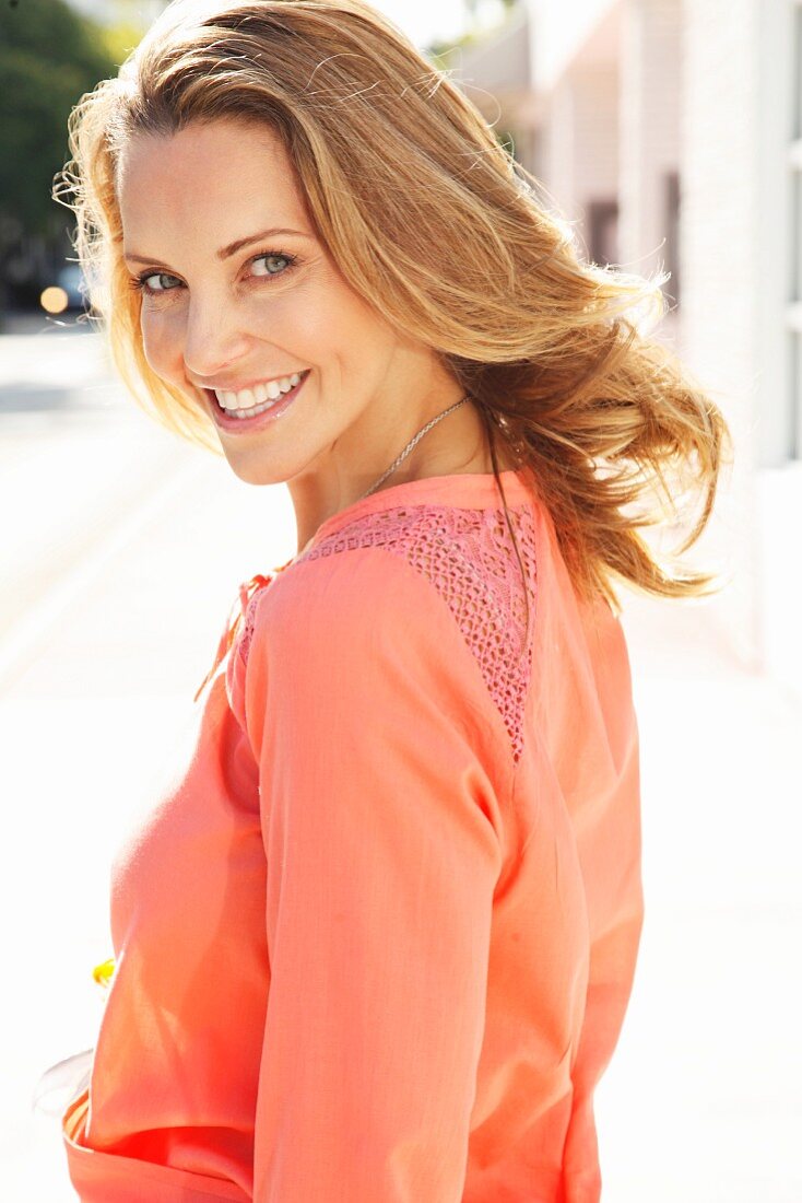 A young blonde woman wearing a salmon pink blouse