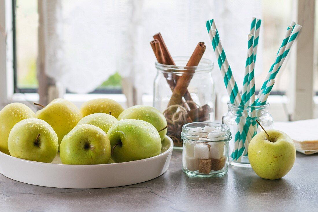 Grüne Äpfel, Zuckerwürfel und Zimtstangen auf dem Küchentisch