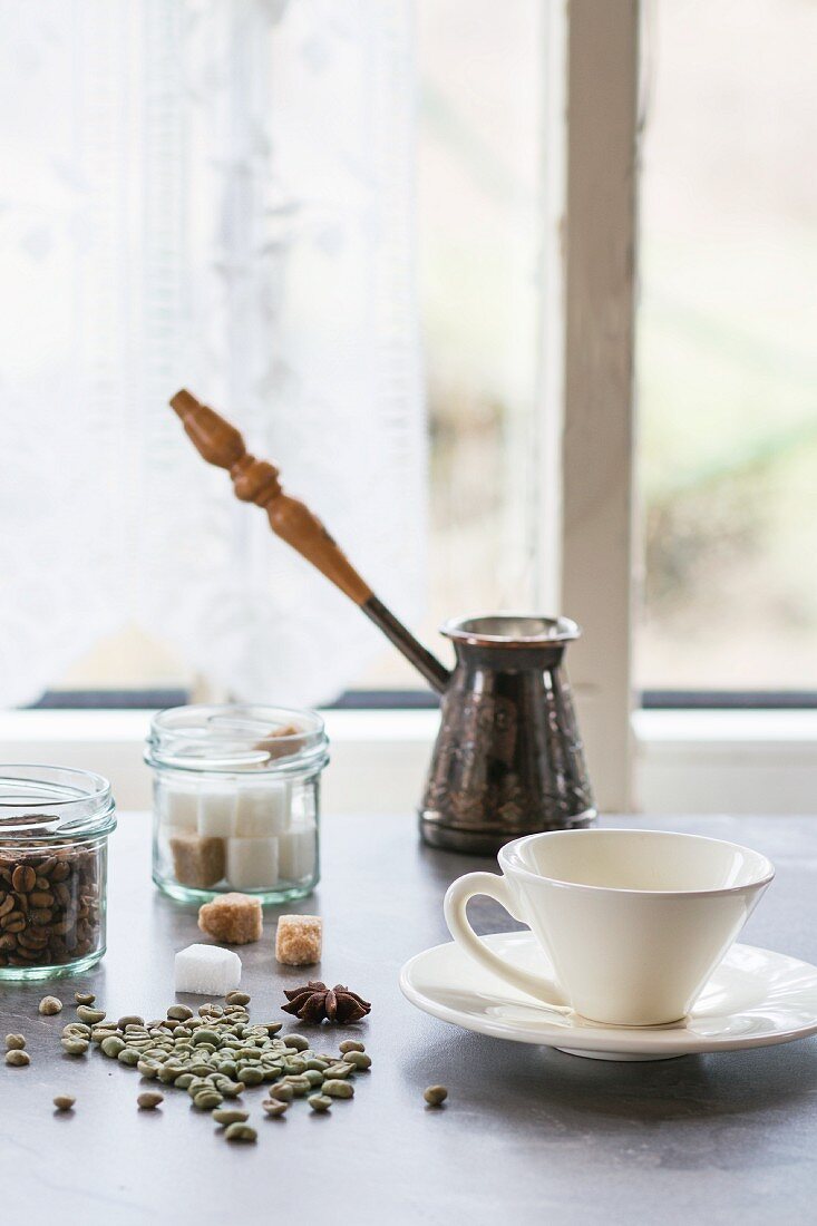 Kaffeetasse, Würfelzucker und ungeröstete Kaffeebohnen auf dem Küchentisch