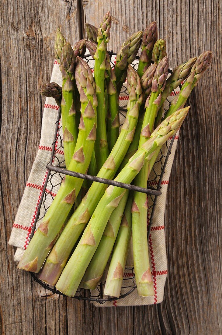 Green asparagus in a wire basket on a tea towel