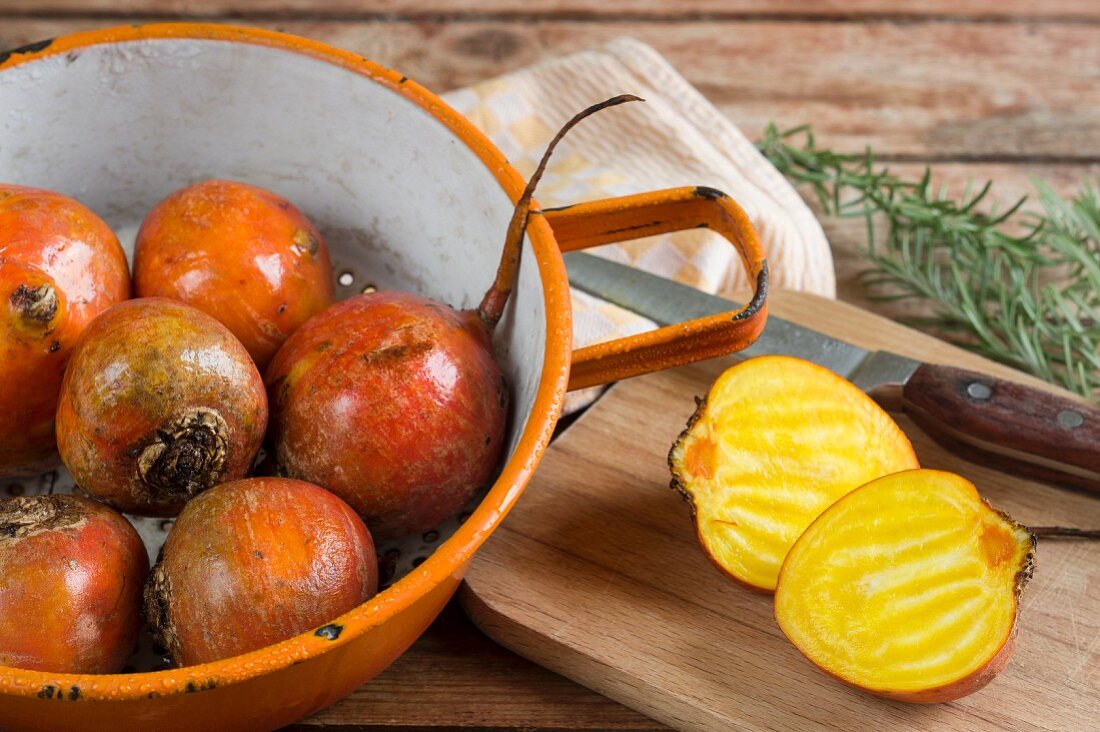 Freshly washed golden beets in a colander and one on a chopping board