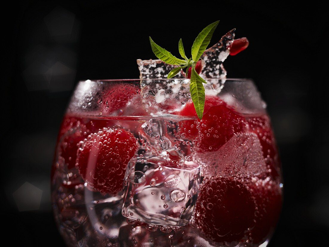 An exotic raspberry drink with whole raspberries, ice cubes and sugar decoration with pomegranate seeds