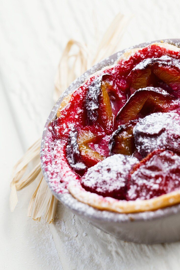 Plum tartlet with icing sugar in a baking dish (close-up)