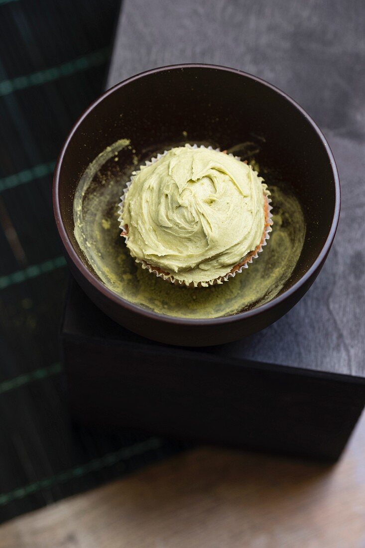 A cupcake with matcha tea frosting in a bowl on matcha powder