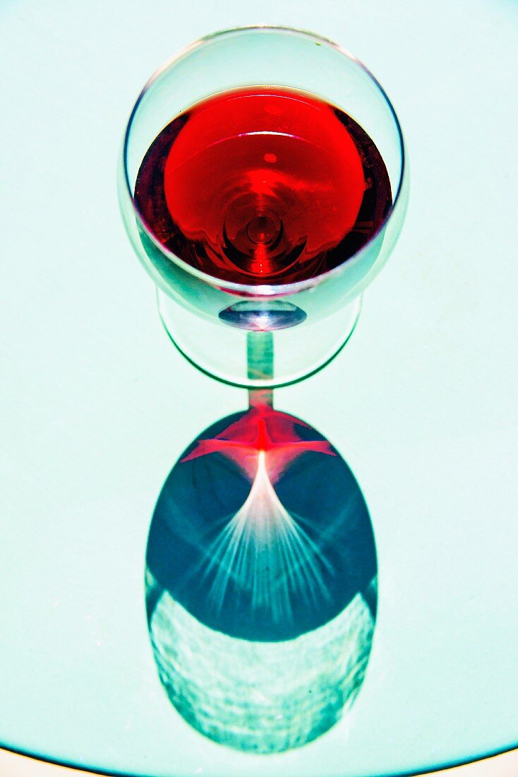 A glass of red wine reflected in a glass table