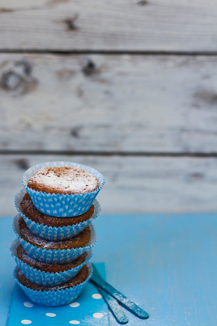 A stack of muffins with icing sugar in blue paper cases