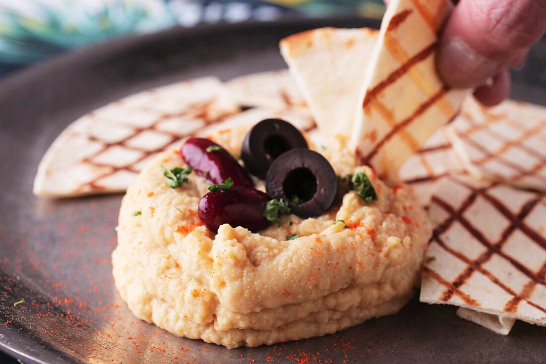 A hand dipping unleavened bread in hummus