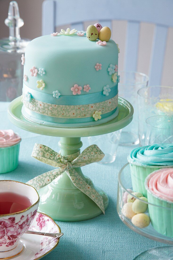 A cake decorated with pastel-coloured fondant on a cake stand for an Easter party