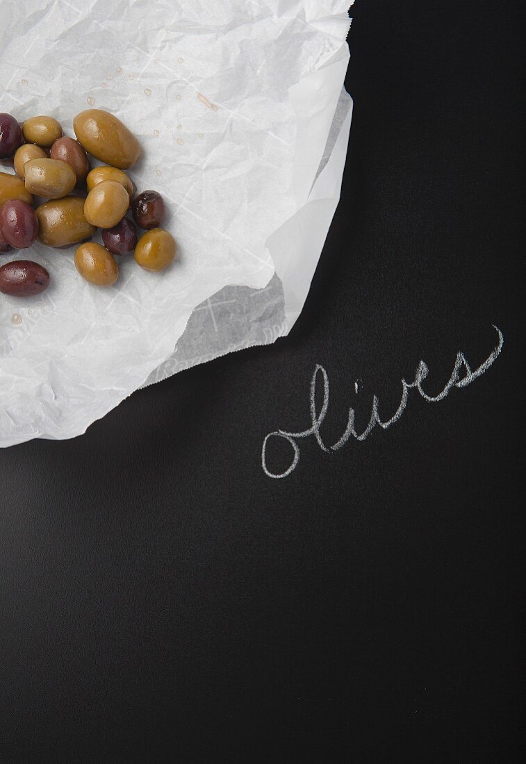 Olives on a piece of paper on a slate surface with a label