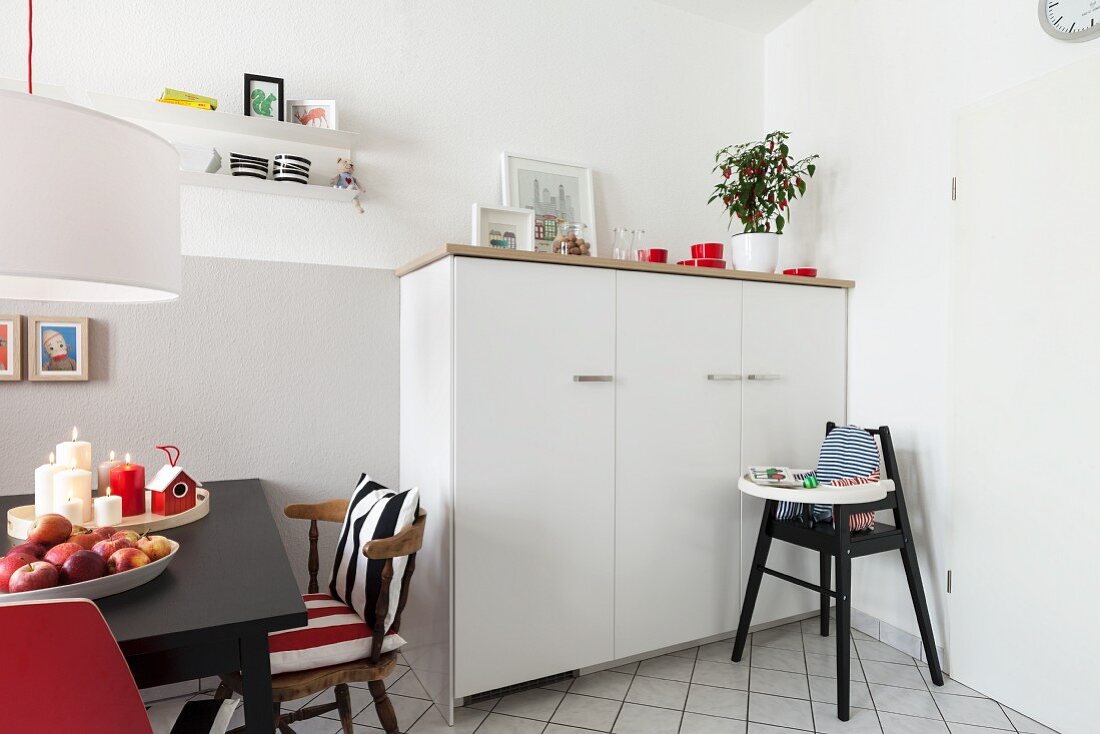 A half-height white cupboard with a highchair in front of it with and eating area to the side with a black table in a renovated living-kitchen area