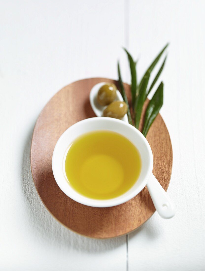 A bowl of olive oil, green olives and a spring of olive leaves