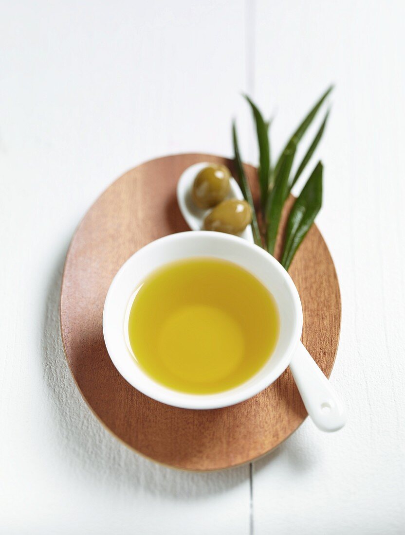 Olivenöl im Schälchen, grüne Oliven und Olivenzweig