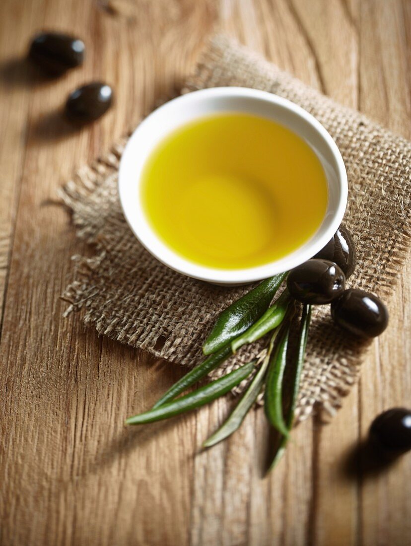 Olivenöl im Schälchen, schwarze Oliven und Olivenzweig