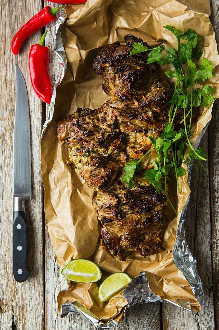 Gebratene aufgeschnittene Lammkeule mit Koriandergrün, Chili und Limetten auf Holztisch