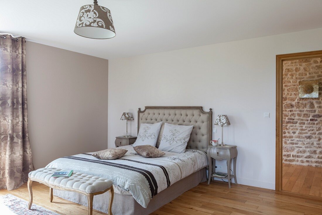 Upholstered, Rococo bench at foot of double bed with button-tufted headboard in simple bedroom