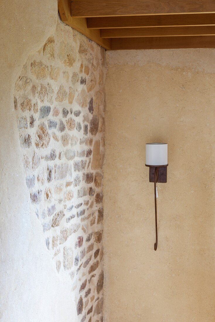 Wrought iron sconce lamp with white lampshade next to stone wall