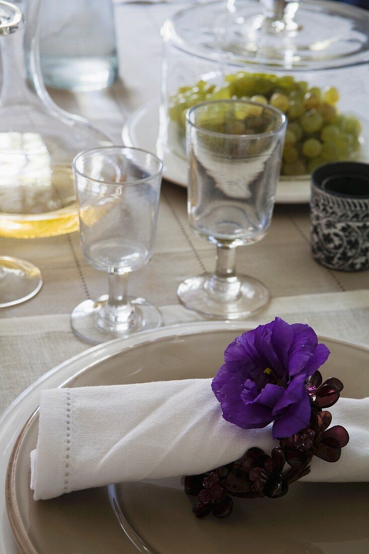 Blaue Anemone mit Blütenring um Leinenserviette auf Tellerset und rustikale Stilgläser