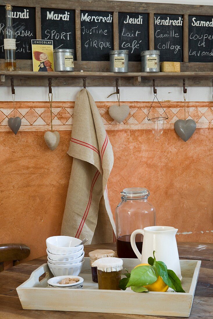 Wandtafel mit Tageseinteilung, Herzendeko und Leinentuch an Haken, Frühstückstablett mit frischen Zitronen im Vordergrund