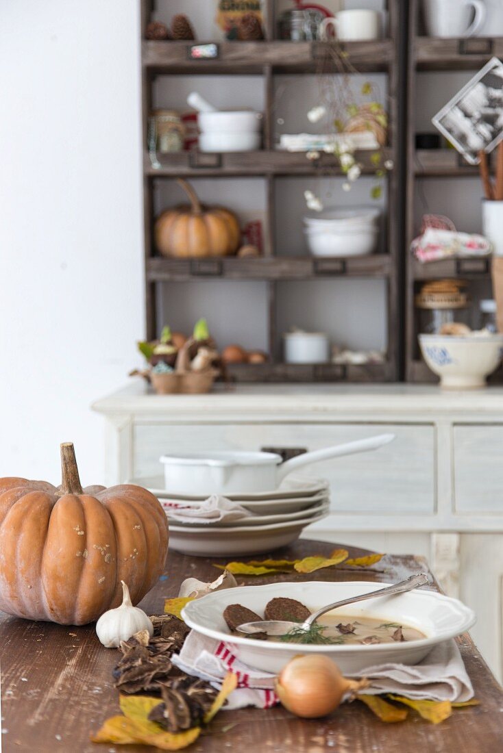 Soup plates and autumn arrangement of leaves and vegetables on kitchen table in rustic interior