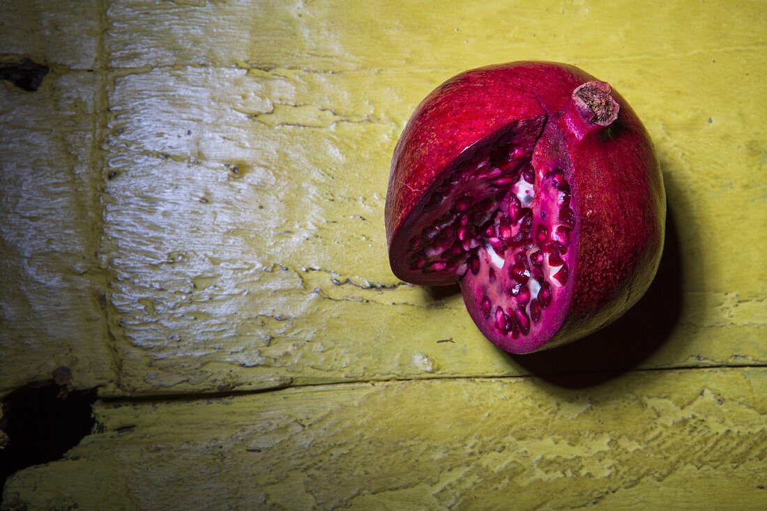 A sliced pomegranate on a rustic yellow wooden surface