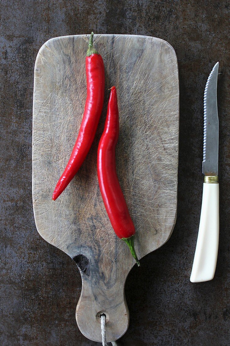 Two red chilli peppers on a chopping board (seen from above)