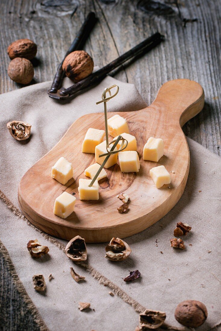 Small cubes of cheese on an olive wood chopping board with walnuts