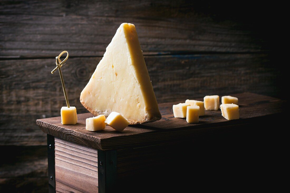 A piece of Belgian cheese and cubes of cheese on a wooden box