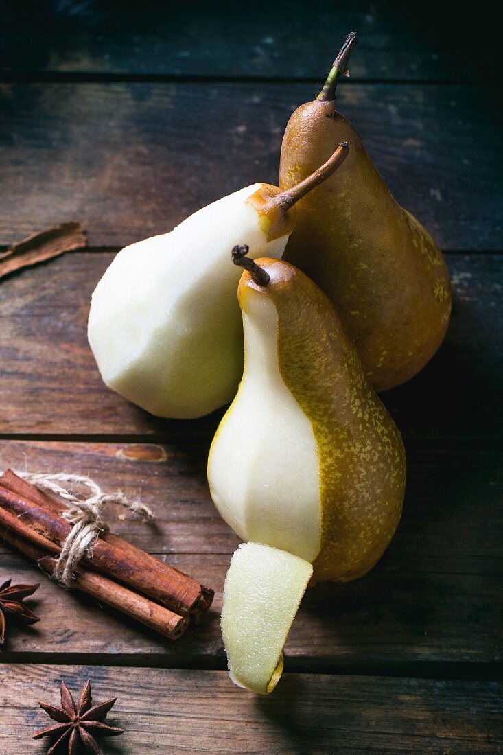 Partially peeled pears with spices on a wooden table
