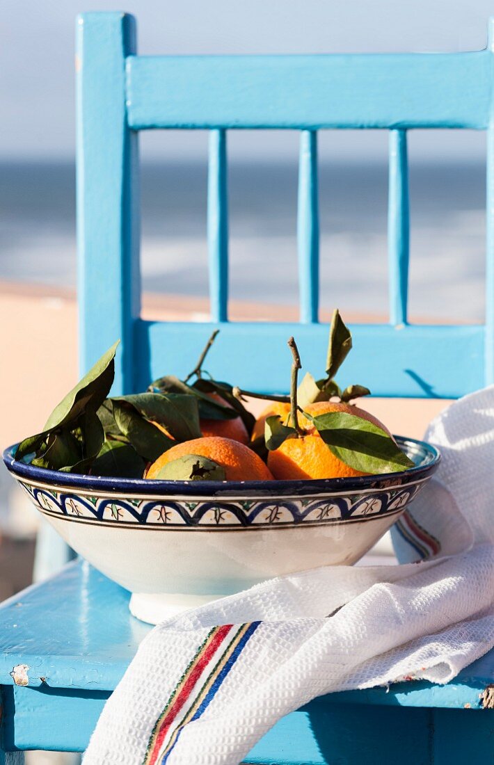 Orangen in einer Keramikschale auf hellblauem Stuhl am Meer