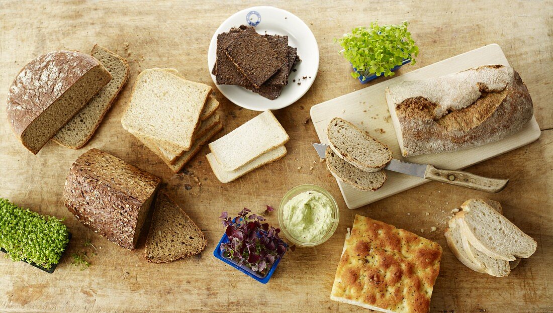 Verschiedene Brote, Kresse und Brotaufstrich auf Holzuntergrund (Draufsicht)