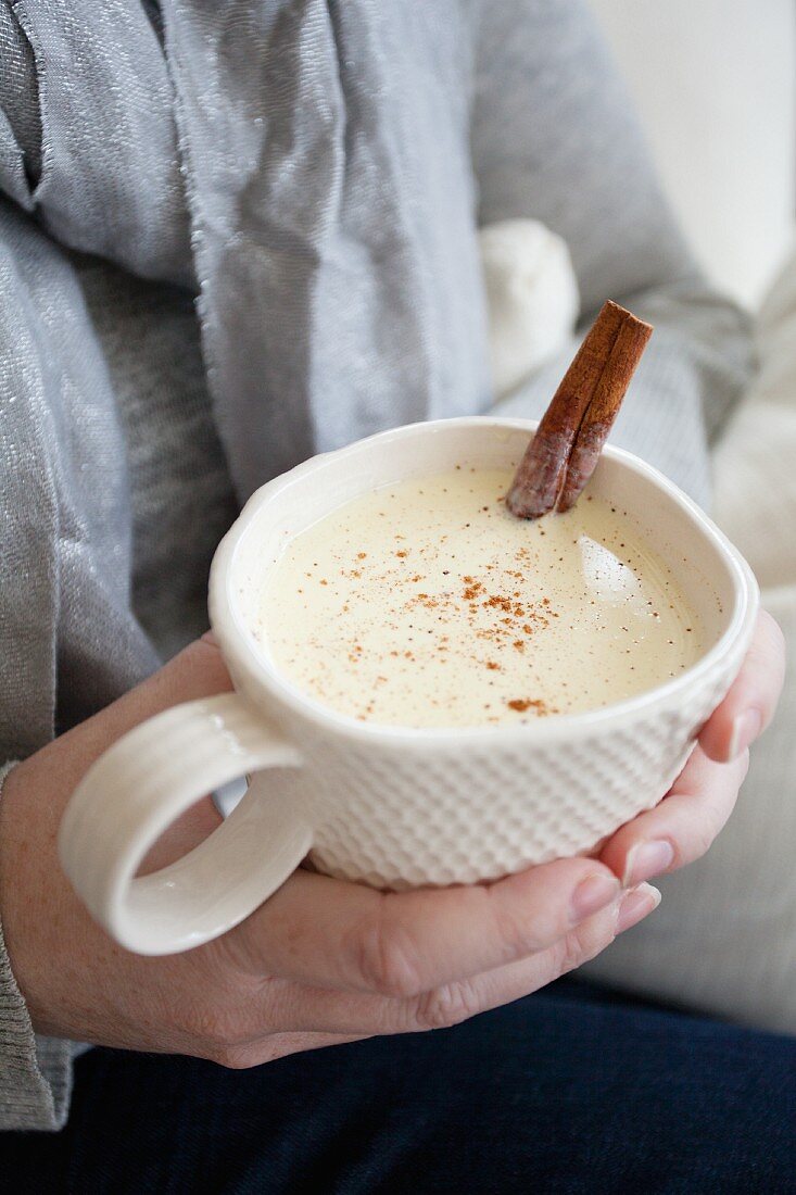 A woman holding a cup of eggnog with cinnamon