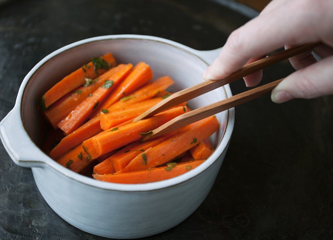 Cooked carrots being removed from a saucepan with a pair of tongs