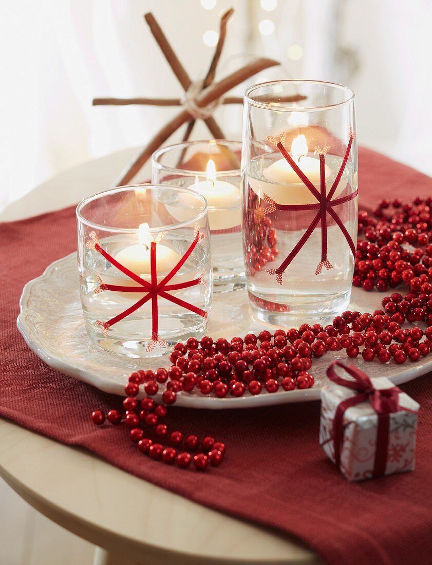 Weihnachtsdekoration - Rote Perlenkette neben Schwimmkerzen auf weisser Schale