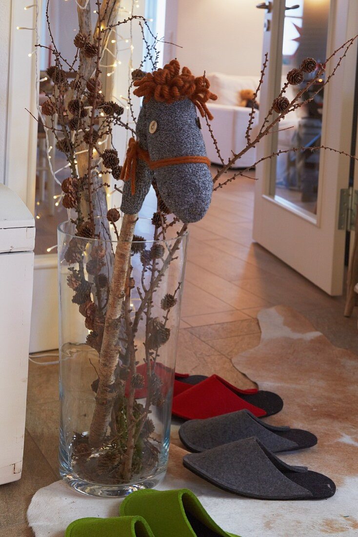 A homemade hobby horse in a vase decorated for Christmas with felt guest slippers on the floor