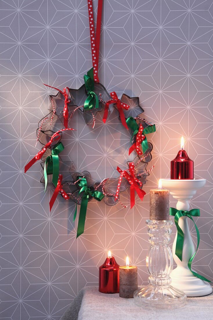 Kranz aus Plätzchenausstechern und Schleifenbändern als weihnachtlicher Wandschmuck, daneben Kerzenständern