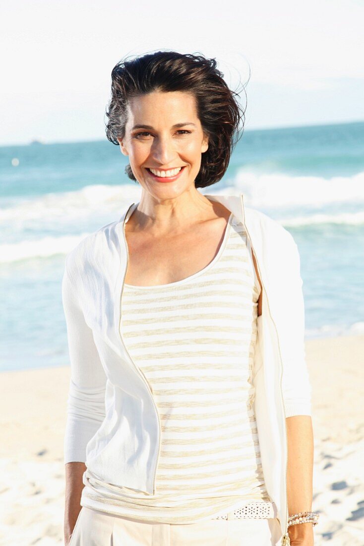 Dunkelhaarige Frau mit hellem T-Shirt und Jacke am Strand