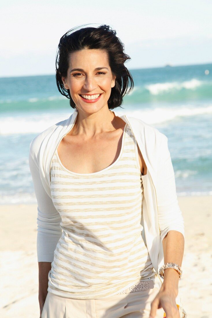 Dunkelhaarige Frau mit hellem T-Shirt und Jacke am Strand