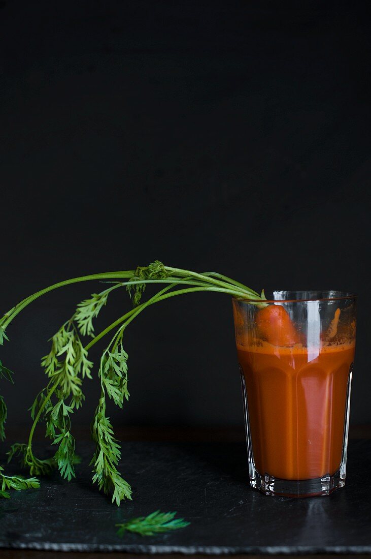 A glass of carrot juice with a fresh carrot