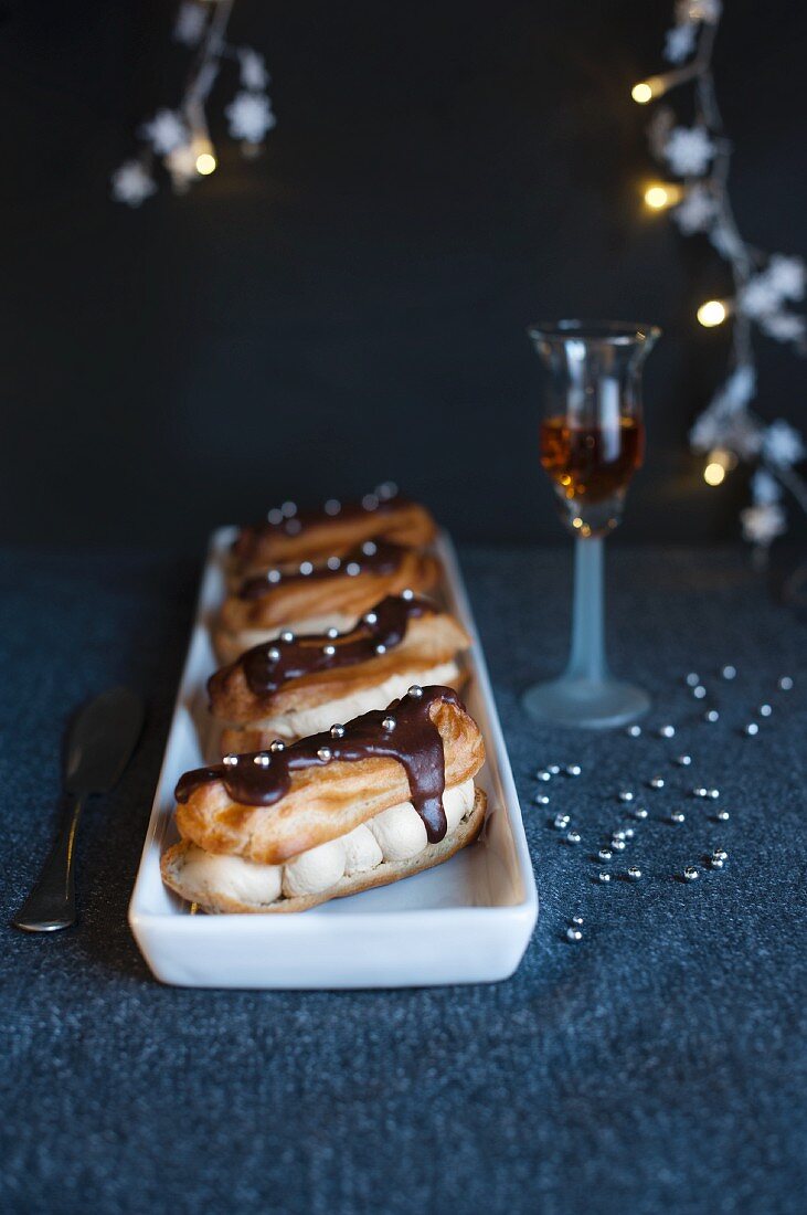 A chocolate covered eclair with silver pearls and coffee cream next to a glass of sherry (Christmas)
