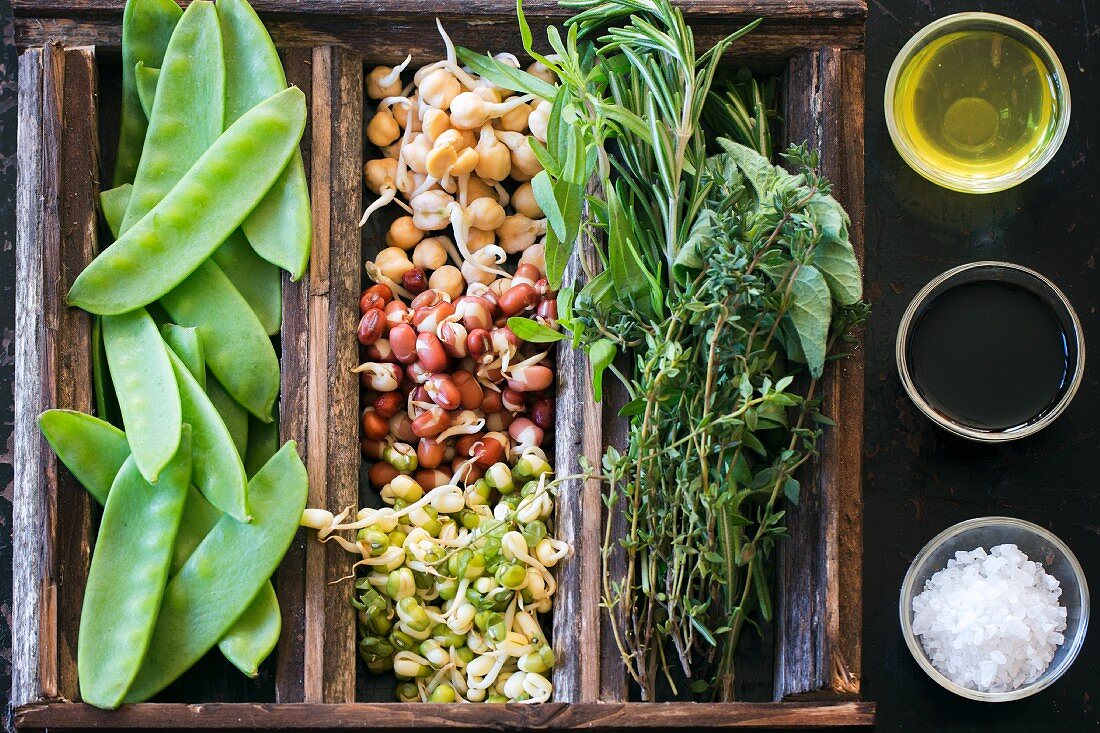 Bean sprouts, mange tout and herbs in a wooden crate next to olive oil, balsamic vinegar and sea salt