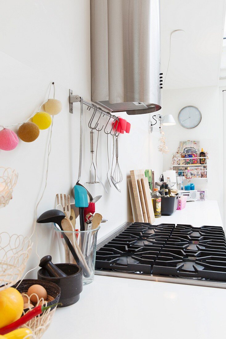 A white kitchen work surface with a gas hob with kitchen utensils and a string of lanterns hanging on the wall