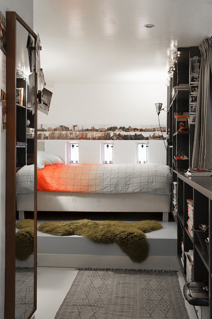 Schlazimmer mit Bett auf Podest, an Wand Regaleinbauten