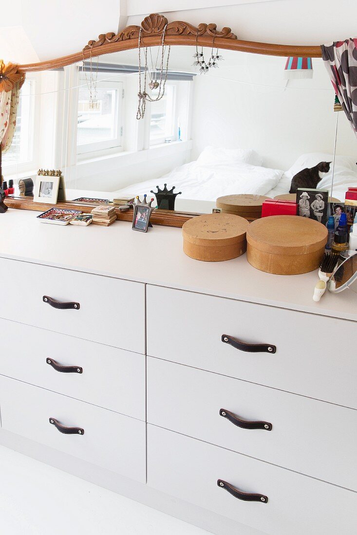 Mirror with carved frame, jewellery and make-up utensils on white chest of drawers