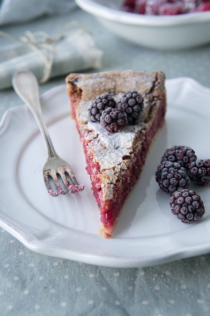 Ein Stück Himbeertarte mit gefrorenen Brombeeren