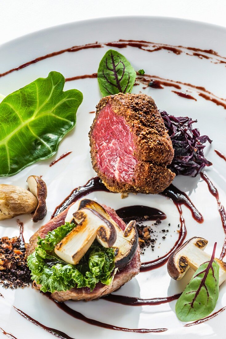 A platter of game with variations of venison with porcini mushrooms, red cabbage and leafy greens