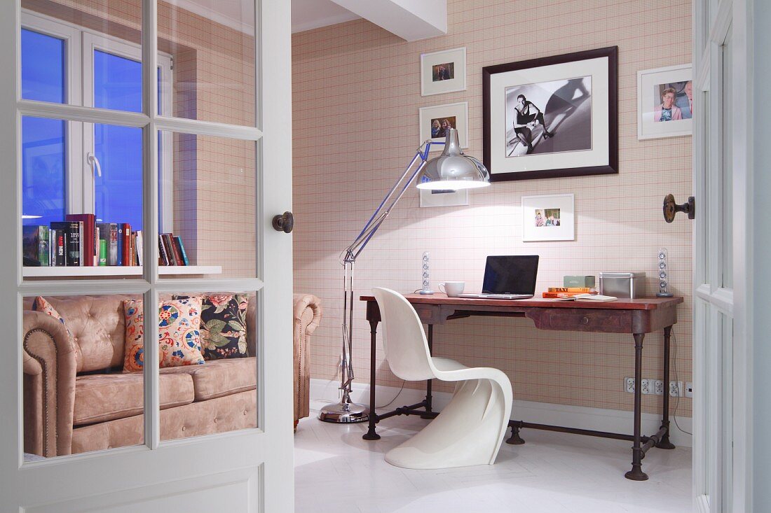 View through open door of workspace with white Verner Panton chair and desk against wall next to retro standard lamp