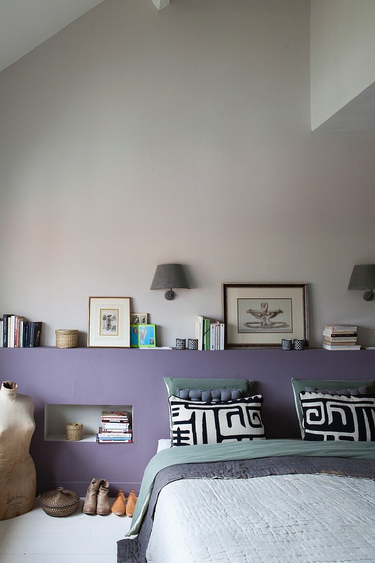 Modern bedroom with lilac headboard wall, stacked books, black and white pillows and vintage tailors' dummy