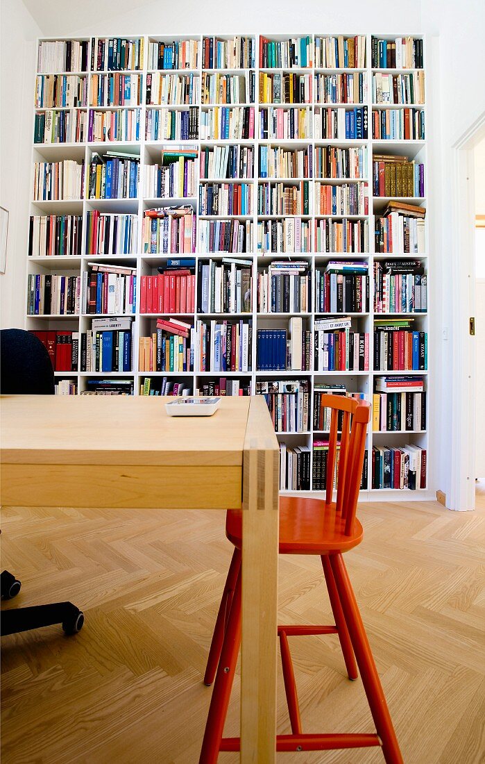 Tisch aus hellem Holz und roter Kinderstuhl, im Hintergrund raumhohe Bücherwand