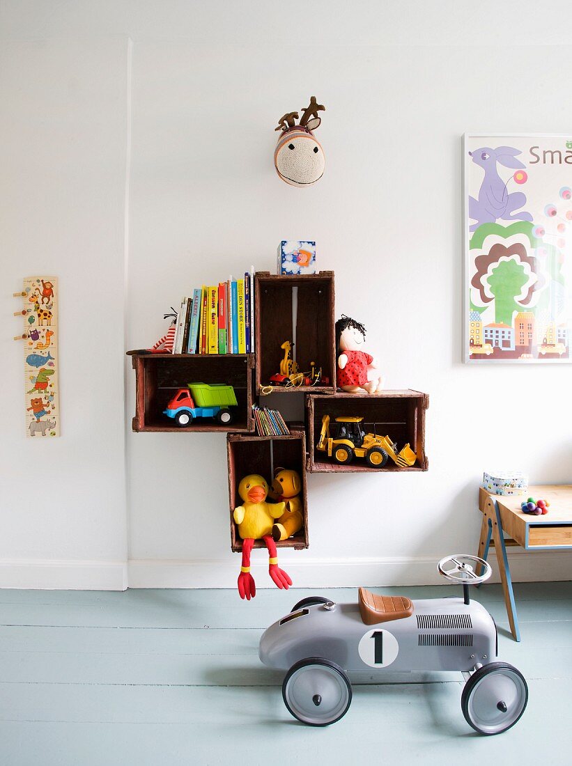 Retro Spielzeugauto auf grauem Dielenboden, an Wand befestigte Holzkisten mit Spielzeug und Kinderbüchern
