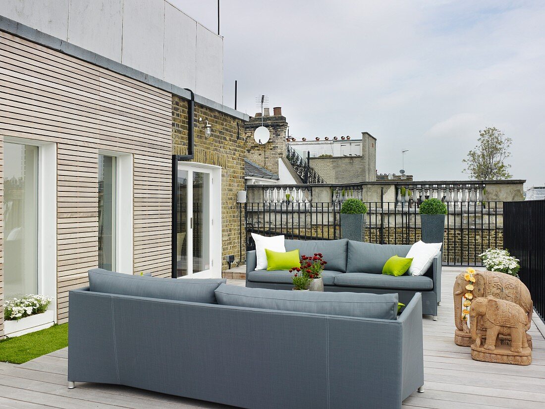 Elegant grey sofas and sandstone elephant ornaments on roof terrace with wooden decking